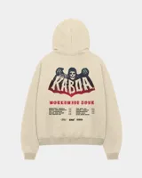 Canguro de felpa color beige con capucha, corte recto y cómodo, con estampa en la espalda con diseño de calavera y texto alusivo a gira mundial.