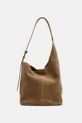 Bolso tipo saca de diseño asimétrico confeccionado en piel de ante. Cuenta con un asa bandolera ajustable, cierre mediante imán y un bolsillo interior con cremallera.