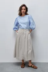 Falda midi color beige de tiro alto y silueta amplia, confeccionada en tela liviana con pinzas en el frente, pasacintos y bolsillos laterales.