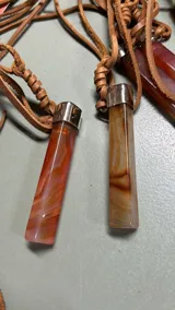 Collar con dije de piedra rectangular con vetas marrones y rojas, engarzado en metal plateado y colgante de tiento de cuero marrón.