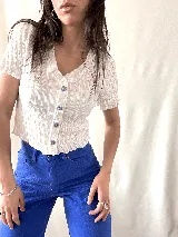 Camisa blanca con textura arrugada, escote en V, mangas cortas con volados y botones con forma de flor.