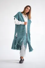 Chaleco largo de tejido de punto color azul verdoso, sin mangas y con flecos en el ruedo. Presenta calados con diseño geométrico.