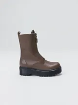 Botas de cuero color marrón de caña alta, con plataforma gruesa de goma y cierre metálico frontal con tirador. Presentan costuras a contratono y detalle de etiqueta de la marca en la lengüeta.
