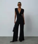 Mono largo de microfibra color negro, con escote en V profundo tipo cruzado, hombreras estructuradas y diseño sin mangas con breteles anchos. Presenta una cintura ajustada y pantalón de corte recto y amplio.
