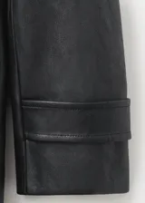 Abrigo largo de estilo trench confeccionado en cuero sintético negro, con diseño recto, cuello con solapa y detalle de cuello de pelo sintético extraíble. Cuenta con cierre frontal de botones, cinturón ajustable con hebilla, bolsillos laterales y mangas largas con trabillas.