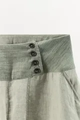 Pantalón bombacho de lino con tiro bajo, cintura ancha a contraste con cierre de botones, bolsillos laterales y bajo abullonado con puño.