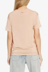Remera de manga corta color beige, con diseño liso de acabado satinado, corte holgado y cuello redondo.