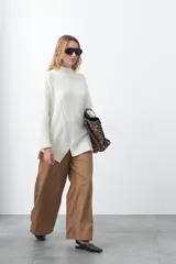 Polera de tejido de punto color marrón, con diseño asimétrico y costura diagonal frontal. Presenta cuello alto, hombros caídos, mangas largas con puños acanalados y ruedo con abertura frontal.