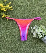 Conjunto de bikini con corpiño triangular fijo y bombacha colaless regulable, con estampado degradado en tonos naranja, rosado y violeta.