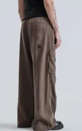 Pantalón cargo de silueta oversize, color marrón oscuro, confeccionado en tejido técnico liviano de poliéster. Presenta cintura elástica y múltiples bolsillos funcionales tipo cargo en las piernas. Incluye un cinturón de cinta negra con hebilla de plástico.