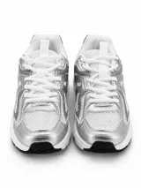 Zapatilla deportiva de estilo urbano con diseño técnico, confeccionada en una combinación de malla blanca y paneles metalizados en color plateado. Presenta cordones blancos, suela con base negra y estructura reforzada.