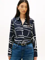 Camisa de Tommy Hilfiger de corte regular, confeccionada en sarga de viscosa azul marino con estampado abstracto de líneas blancas. Presenta cuello inglés, cierre frontal oculto con botones dorados, mangas largas con puños abotonados y detalle de plisado en la espalda.