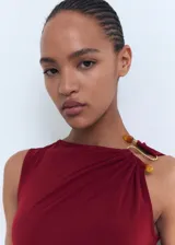 Vestido midi entallado de color bordó, sin mangas, con cuello redondo y detalle drapeado en el lateral de la cintura. Presenta una joya decorativa en uno de los hombros.