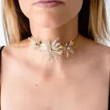 Gargantilla dorada con tres flores de mostacillas blancas y circonitas en el centro.