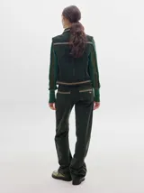 Chaleco de pana negro con cierre frontal de botones metálicos dorados. Presenta detalles de costuras en contraste en el cuello, cartera y canesú, e incluye un pequeño parche con forma de bandera en el pecho.