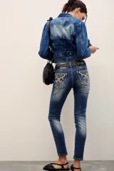 Pantalón jean de corte chupín, tiro medio y lavado azul con efecto gastado. Cuenta con bolsillos traseros con bordados ornamentales y tachas metálicas.