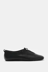 Zapato plano tipo bailarina confeccionado en piel con textura granulada. Presenta cierre mediante lazo en la parte delantera, punta redonda y tirador en la parte trasera.