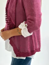 Sweater de punto color magenta con diseño asimétrico, cuello redondo y detalle de encaje bordado en el frente. Incluye una bufanda del mismo tejido y color, y se presenta superpuesto sobre una camisa blanca de algodón.