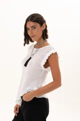 Blusa de textura rugosa en color blanco, sin mangas, con detalle de volados en los hombros y corte asimétrico en el ruedo.