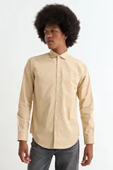Camisa de manga larga en color beige, confeccionada en algodón, con cuello clásico y cierre frontal de botones.