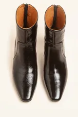 Bota de caña corta confeccionada en cuero vacuno color chocolate con acabado brillante. Presenta punta fina, cierre posterior y taco chupete bajo.