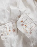 Blusa de lino color salmón con cuello alto, mangas abullonadas y detalle de alforzas en el frente. Presenta terminaciones con puntilla ondulada negra y cierre posterior con botones a la vista.