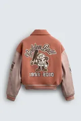 Cazadora tipo varsity de corte cropped, con cuerpo en tejido azul y mangas en contraste efecto piel color beige. Presenta cuello solapa, cierre frontal con botones a presión, bolsillos de vivo y acabados en rib a rayas. Incluye parches y bordados decorativos en el frente, espalda y mangas, con interior acolchado.