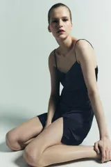 Vestido corto de tejido satinado color azul marino, con escote pico y tirantes finos. El bajo tiene una abertura frontal.