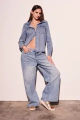 Camisa de denim celeste con cuello clásico, cierre frontal con botones a presión, dos bolsillos con solapa abotonada en el pecho y mangas largas con puños abotonados.