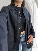 Sobrecamisa negra de jean con cuello camisero, cierre frontal con botones metálicos, bolsillos de parche en el pecho y corte recto.