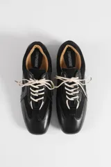 Zapatillas negras de estilo urbano con cordones blancos, confeccionadas en cuero sintético y poliéster, con diseño de paneles y suela plana.