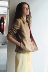 Blazer de cuero color beige con cuello solapa, manga larga y cierre frontal con cremallera y botones a presión ocultos. Presenta bolsillos laterales ocultos en costura y forro interior.