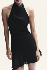 Vestido corto negro de tejido fluido con cuello halter que se ata con lazada. Tiene forro interior, detalle de frunces y bajo asimétrico con volantes. Cierre lateral con cremallera oculta.
