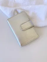 Tarjetero plateado de cuero con broche a presión. Tiene espacio para 4 tarjetas y billetes, y un bolsillo externo.