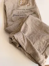 Pantalón de corte relajado color beige, con cintura elástica y cordón ajustable. Presenta parches decorativos con lentejuelas y tachas en los muslos, además de detalles de texto estampado. Posee bolsillos laterales y dobladillo en los tobillos.