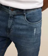 Pantalón skinny de jean nevado para hombre, confeccionado en denim de algodón con elastano. Presenta un lavado azul medio con ligeros desgastes y calce ajustado.
