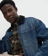 Campera de jean de corte oversized, con cuello de terciopelo, cierre frontal por botones y bolsillos grandes aplicados en el frente.