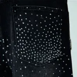 Short de jean negro con tachas plateadas, corte recto y largo hasta la rodilla.