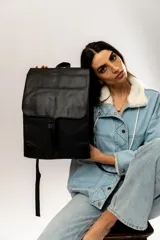 Mochila negra de cuero sintético con solapa superior y cierre con hebilla.