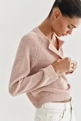 Sweater de punto color beige con cuello redondo, manga larga y cierre frontal parcial con botones. Presenta terminaciones en rib en cuello, puños y dobladillo.