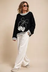 Sweater de punto negro con diseño frontal bordado de cerezas con moño en color blanco, y detalles de líneas blancas en cuello, puños y ruedo.