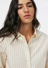 Camisa de corte clásico con cuello camisero, manga larga con puños vueltos y cierre frontal de botones. Presenta un diseño de rayas verticales finas en tono beige.