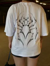 Remera blanca oversize de manga corta, con cuello redondo y diseño gráfico de araña en el pecho.