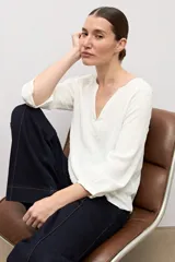 Blusa blanca de tejido plumeti con escote en V y mangas tres cuartos.