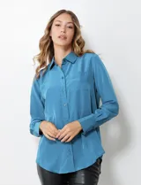 Camisa de satén color violeta, con cuello clásico, cierre frontal con botones, manga larga con puños anchos abotonados y bolsillo aplicado en el pecho.