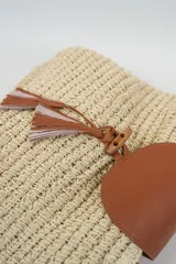 Bolso tipo tote color beige de tejido rústico, con asas de hombro, solapa frontal y detalle de borlas colgantes en tonos marrones y rosados.