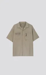 Camisa de manga corta color beige, estilo técnico, confeccionada en microfibra liviana. Cuenta con doble bolsillo frontal, uno con detalle de malla y otro con cierre, y broches en lugar de botones.