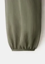 Vestido midi color verde militar, confeccionado en tejido fluido de poliéster. Presenta un diseño evasé, escote de pico con volantes, y mangas largas con puños elásticos. Incluye detalles de volantes en el cuello y forro interior.