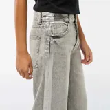 Jean de corte baggy en color gris con efecto lavado ácido. Presenta bandas laterales en tono plateado brillante y diseño de cinco bolsillos con cierre de botón y cremallera.