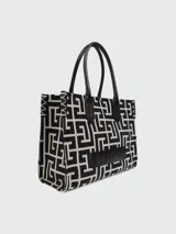 Tote bag Balmain de tamaño pequeño con estampado de monograma geométrico en blanco y negro. Presenta asas de cuero negro, detalles de costuras en contraste en los laterales y una placa de cuero con el logo de la marca grabado en la parte frontal.